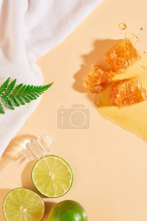 Téléchargez les photos : Cire d'abeille décorée de plusieurs tranches de citron vert et d'un miel qui dégouline. Serviette blanche exposée. Le miel peut apaiser la peau sèche, irritée et ridée - en image libre de droit