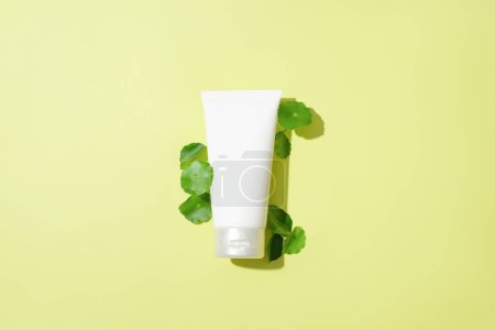 Photo for A cosmetic tube is dotted with the green color of pennywort leaves on a pastel background. Centella asiatica extract helps maintain skin moisture - Royalty Free Image
