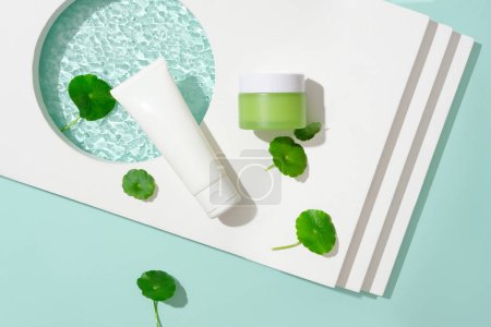 Photo for A white tube, a green lotion jar, a podium, and pennywort. Notably, Gotu kola possesses the remarkable capability to stimulate collagen production, contributing to skincare and wellness. - Royalty Free Image