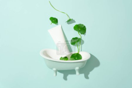 Photo for Close-up of a plastic tube placed next to pennywort leaves and a mini bathtub. Creative space for cosmetic advertising with pennywort extract. Copy space. - Royalty Free Image