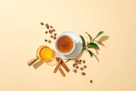 Foto de Una taza de té, canela, hojas de té verde, hierbas y miel sobre un fondo pastel. La combinación de miel e ingredientes naturales es muy buena para la salud. - Imagen libre de derechos
