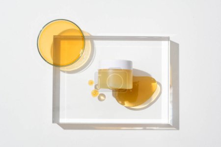 Téléchargez les photos : Gros plan d'un pot de cosmétiques sans marque affiché sur une plate-forme en verre transparent avec des gouttes de miel. Le miel est utilisé comme un très bon hydratant pour la peau. - en image libre de droit