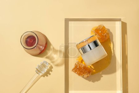 Foto de Un frasco cosmético con un diseño lujoso se coloca en un podio de vidrio. La miel se almacena en un frasco de vidrio y una llovizna de miel sobre fondo beige. Concepto cosmético. - Imagen libre de derechos