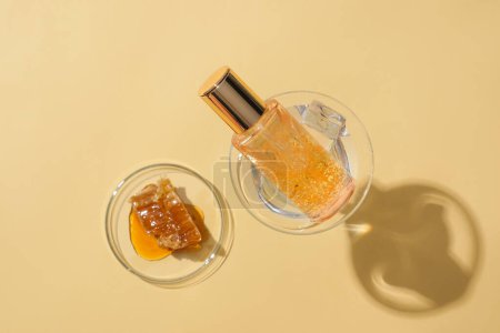 Téléchargez les photos : Gros plan d'une bouteille de sérum placée dans un verre à cocktail, cire d'abeille sur une boîte de Pétri sur un fond minimaliste. Le miel contient des antioxydants, des enzymes et d'autres nutriments qui aident à nettoyer la peau. - en image libre de droit
