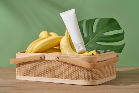 Foto de Una gran cesta llena de plátanos amarillos con un tubo cosmético puesto en la parte superior. Banana (Musaceae) contiene aminoácidos, que son los ingredientes perfectos para una mejor elasticidad de la piel - Imagen libre de derechos