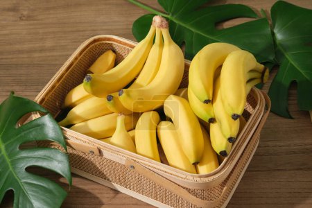 Téléchargez les photos : Les bananes sont disposées à l'intérieur d'un panier en bambou décoré de feuilles vertes fraîches. Banane (Musaceae) protégera le corps contre les dommages causés par l'oxydation des radicaux libres - en image libre de droit