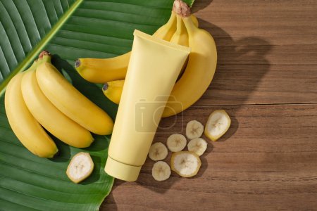Cosmetic container in yellow color displayed with banana bunches and slices. Banana (Musaceae) is loaded with antioxidants that can help reduce inflammation in the skin
