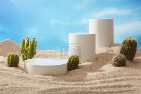 Téléchargez les photos : Trois podiums blancs ronds et cylindriques sont exposés sur le sable de plage avec des cactus. Espace vide pour promouvoir le produit - en image libre de droit