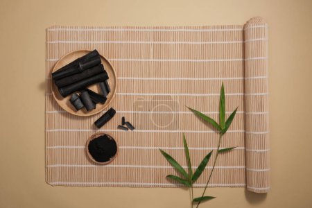 Photo for Minimal style, advertising photo for cosmetics product from bamboo charcoal extract. Top view of bamboo charcoal on wooden plate and green leaves decorated on brown bamboo mat - Royalty Free Image