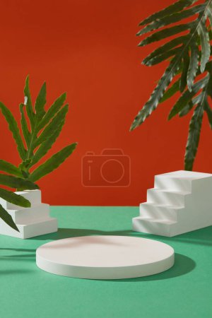 Téléchargez les photos : Podium rond, petit escalier blanc et feuilles vertes décorées sur fond orange. Scène pour la présentation des produits d'été. Vue de face, photo publicitaire avec des plantes naturelles - en image libre de droit