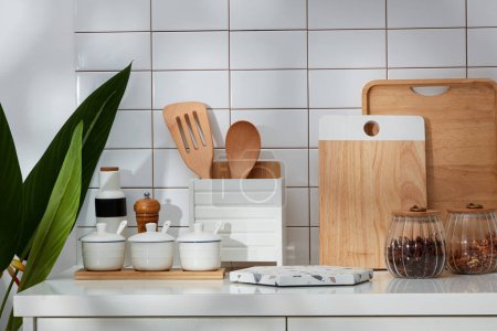 A corner of a modern kitchen with full kitchen appliances and green plants on a white tile wall background. In the middle is an empty marble podium for product presentation.