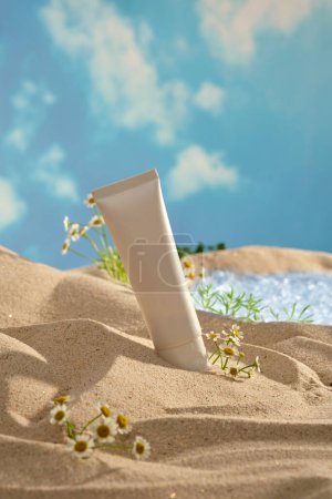 Mockup-Szene für Werbekosmetik mit natürlichem Konzept. Ein leerer weißer Plastikschlauch auf Sand mit frischem Mutterkraut und einem kleinen See vor blauem Himmel. Raum für Design