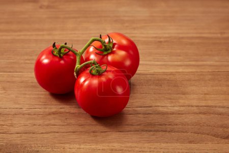 Photo for Some fresh tomatoes with green petiole on wooden background. Scene for advertising and branding product with copy space. Eat a lot of tomatoes to help brighten the skin, anti-oxidant and prevent acne - Royalty Free Image