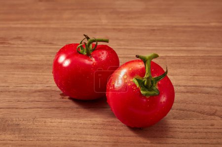 Photo for Two fresh-picked tomatoes with green stems are placed on a rustic wooden background. Tomato bring many health benefits, high nutritional content and help the body fight many diseases. - Royalty Free Image
