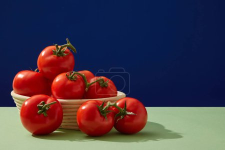 Photo for Front view of round basket containing a lot of fresh tomatoes on a dark blue background. Blank space for display cosmetic product with ingredient from tomato. Copy space - Royalty Free Image