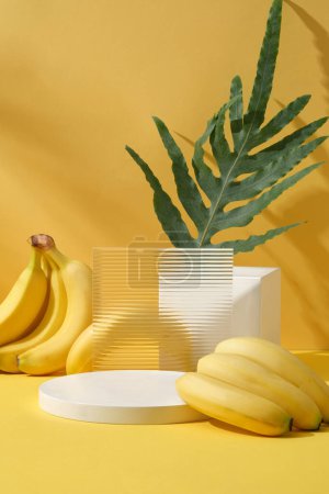 Photo for Background for display cosmetic of natural extract - fresh ripe bananas and green leaf arranged on yellow background with empty white podiums. Advertising and branding cosmetic product - Royalty Free Image