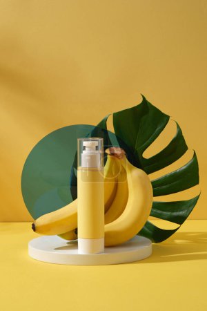 Téléchargez les photos : Une bouteille de pompe vide placée sur un podium rond avec des bananes fraîches et des feuilles vertes sur fond jaune. Mockup pour le design, cosmétiques bio, concept de produits de beauté - en image libre de droit