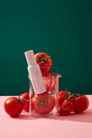 Vista frontal de una botella de plástico vacía colocada en un vaso de precipitados con tomates maduros frescos sobre un fondo de color. Escena para publicidad cosmética de extracto de tomate con embalaje en blanco maqueta