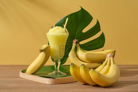 Téléchargez les photos : Bananes fraîches mûres avec tasse de smoothie et feuille verte sur fond jaune. Manger des bananes tous les jours est un moyen simple mais extrêmement efficace pour embellir la peau. Photo publicitaire - en image libre de droit