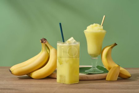 Photo for Concept for advertising product with banana ingredient. Ripe bananas and glasses of juice and banana smoothie on a wooden table. Bananas are one of the most consumed fruits in the world - Royalty Free Image