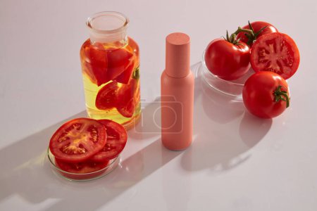Vor weißem Hintergrund eine rosafarbene Kosmetikflasche mit frischen Tomaten, Tomatenscheiben und Laborgläsern. Raum für Design. Tomaten sind ein wichtiger Bestandteil in Schönheitsrezepten