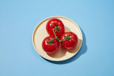 Top view of fresh tomatoes placed on a round plate on a blue background. Advertising scene. Salad preparation ingredients. Empty copy space for mockup