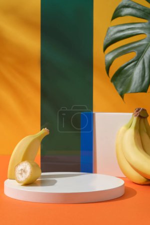 Photo for Front view of round podium with ripe banana, green monstera leaf and acrylic sheet arranged on a yellow background. Blank space for display cosmetic or product with ingredient from banana - Royalty Free Image