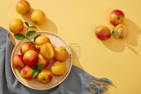 Photo for Fresh peaches (prunus persica) still green petioles decorated on yellow background with gray cotton towel. Scene for advertising cosmetic product of peach extract and copy space. - Royalty Free Image