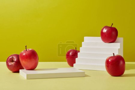 Photo for Product and promotion concept for advertising cosmetic product of apple extract. Some ripe red apples decorated on a green background with rectangle white podium and white stairway. Front view - Royalty Free Image