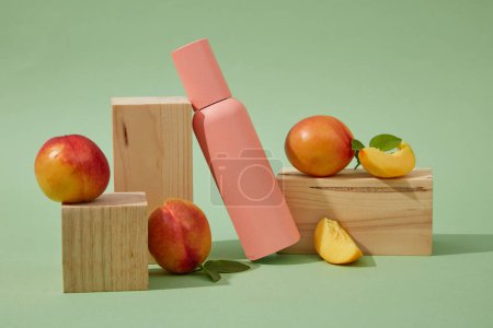 Photo for Mockup scene for advertising and branding cosmetic of peach (prunus persica) extract. A pink cosmetic bottle decorated with fresh peaches and wooden blocks on a green background. Space for design - Royalty Free Image
