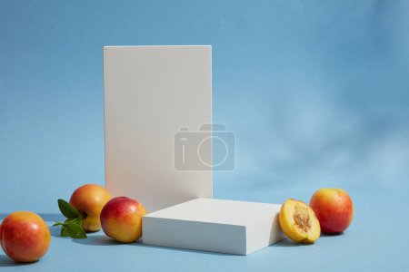 Photo for Minimal background for display cosmetic product of peach (prunus persica) extract. Cylinder white podiums, fresh peaches and green leaves arranged on a blue background with white cloudy - Royalty Free Image