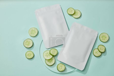Facial sheet cucumber mask package mockup and fresh cucumber slices decorated on pastel background. Antioxidant, anti-aging, and UV protection cucumber face mask