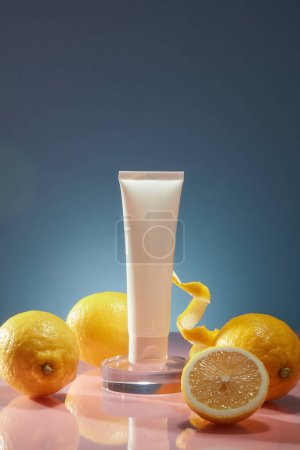 Téléchargez les photos : Vue de face d'un tube en plastique blanc sans marque décoré d'une tasse et d'une bouteille en verre, d'une tranche et d'une écorce de citron sur fond bleu foncé. Maquette pour cosmétique, espace de copie - en image libre de droit