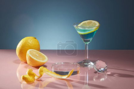 Photo for Peel and slices of fresh lemon are decorated on dark blue background with glass cup and crystal ball. Empty space on transparent podium for display products of lemon extract. Advertising photo. - Royalty Free Image