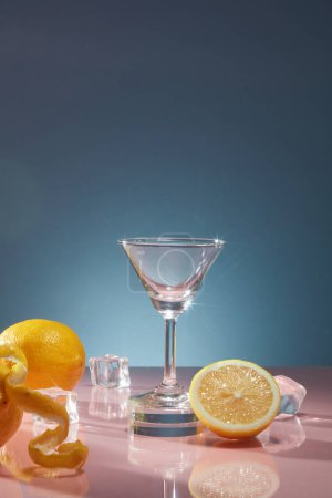 Foto de Copa de vidrio con hielo y limones frescos decorados sobre fondo azul oscuro. Escena para la publicidad de productos de bebidas con sabor a limón fresco para una sensación refrescante - Imagen libre de derechos
