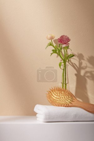 Téléchargez les photos : Concept minimal avec serviette en coton blanc, peigne en bois et un vase de fleurs roses sur fond beige. Espace pour le produit d'affichage. Soins de la peau, concept beauté et spa. - en image libre de droit