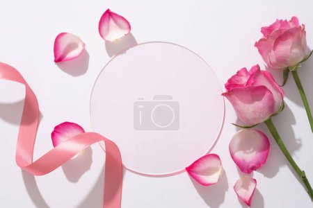 Téléchargez les photos : Fond de beauté avec feuille acrylique ronde forment un espace vide pour le produit d'affichage, roses fraîches, ruban et pétales de rose décorés sur fond blanc. - en image libre de droit