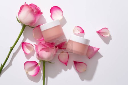 Téléchargez les photos : Pot cosmétique pour soins de la peau à partir d'ingrédients naturels décorés de pétales de rose et de rose sur fond blanc. Espace pour le design, l'emballage de maquettes pour la marque cosmétique. Vue de dessus, plan plat - en image libre de droit
