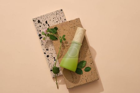 Top view of green glass bottle without label placed on two bricks on beige background. Mock up organic cosmetic with green leaves. Minimal style, space for design