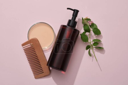 Photo for A amber pump bottle with comb, petri dish filled liquid and lantana camara on pink background. Mockup for shampoo of natural extract. Tropical herbal ingredients good for strong and smooth hair - Royalty Free Image