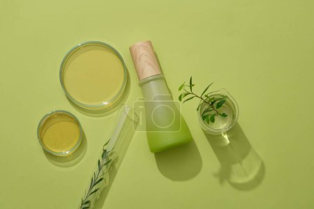 Mockup scene for advertising product with natural extract. Glass bottle unlabeled decorated with lab glassware containing essence and green leaf on green background