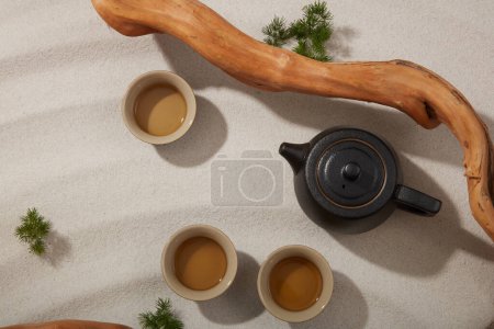 Foto de Vista superior de la tetera negra y el juego de té decorado con ramita seca y hierba verde sobre fondo de arena beige. Antecedentes mínimos para la presentación del producto - Imagen libre de derechos