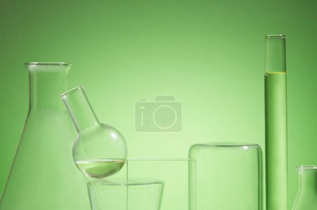 Photo for Front view of lab glassware containing yellow liquid, decorated on green background. Blank space for display product. Concept of research and development of cosmetics with natural extracts - Royalty Free Image