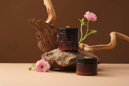 Photo for Front view of two amber jars on stone, pink flowers and dried twigs are decorated on brown background. Minimal concept, mockup for scrub or mask product. Space for design - Royalty Free Image