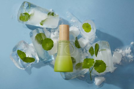 Photo for Mockup of natural cosmetic for the body and face placed on frozen gotu kola leaves in ice cubes on blue background. Green bottle with blank label for show your design - Royalty Free Image