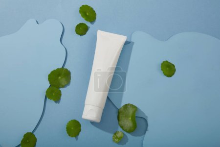 Photo for Minimal concept for advertising cosmetic with white plastic tube container lotion or cleanser on blue background with fresh gotu kola leaves. Cosmetic product mockup extract from gotu kola, copy space - Royalty Free Image