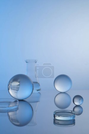 Foto de Petri platos y erlenmeyer matraz llenado de líquido transparente, bolas transparentes y reflexión sobre fondo azul. Espacio en blanco para mostrar producto o texto y diseño. Copiar espacio - Imagen libre de derechos