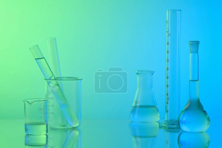 Laboratory concept with lab glassware - erlenmeyer flask, test tubes and beaker filled colorless liquid on gradient background. Space for display product. Minimal style.