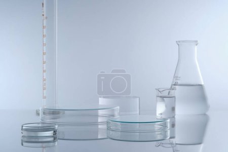 Minimal background with laboratory glassware containing colorless liquid decorated on white background. Two petri dishes upside down form empty platforms to cosmetic product presentation. Front view.