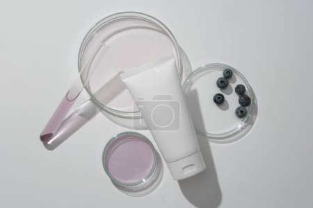 Cleansing and moisturizing tube cosmetics on white background with lab glassware, fresh blueberries and essence. Scene for advertising, space for design. Minimal style